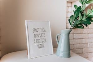 Framed quote 'Start each day with a grateful heart' next to a vase indoors.